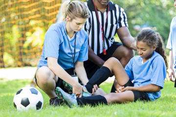 Athletic trainer aiding female athlete with referee