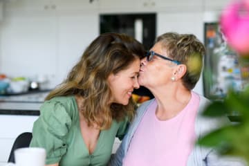 Senior mother kissing adult daughter on her forehead