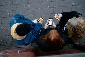 Three friends looking at examples of new media on phones