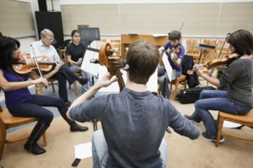 Orchestra students playing string instruments in a classroom