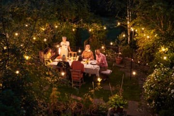 Friends having dinner together outdoors with clear lights in the trees