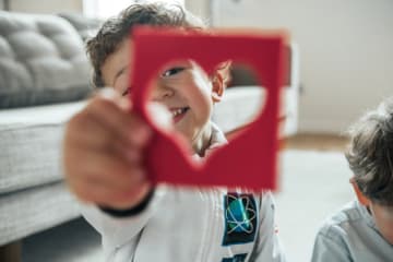 Little boy holding up heart cut out of paper