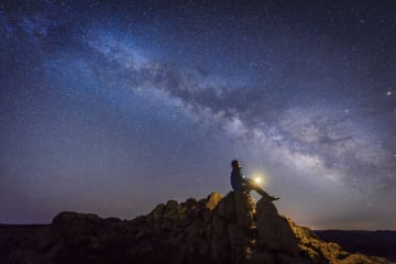 Man sitting on rocks looking up at the stars with beautiful starlit sky above him