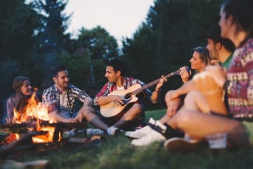 Friends gather and sing around a camp fire