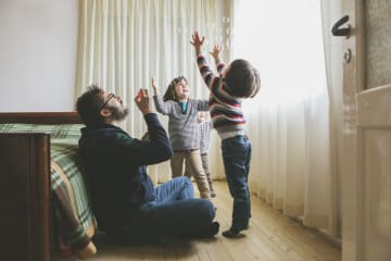 Two young boys play enthusiastically with dad blowing bubbles in bedroom