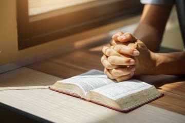 Hands clasped together on top of a Bible