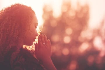 Woman praying outdoors with hands clasped as the sun sets