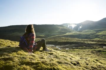 Woman sits on a grassy hill overlooking other grassy hills