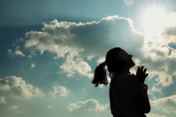 Woman smiles looking up to the sun with clouds in the sky behind her