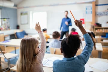 young students raising hands in class