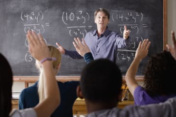 male teacher in front of chalkboard teaching students
