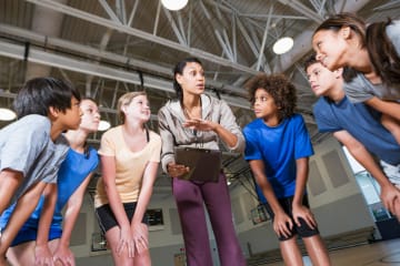 A PE teacher in a huddle with a group of her students