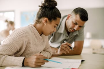 female student and male teacher reading together in classroom