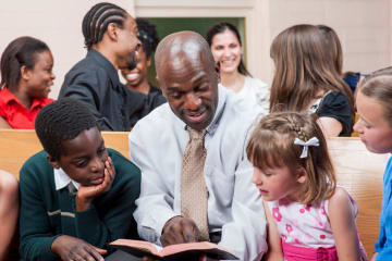 Diversity in the church with African-American man pointing in Bible to children