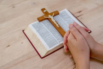 Praying hands are accompanied by a cross and Bible