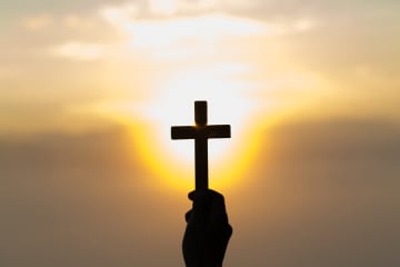 Man holding cross in hand against sunset sky