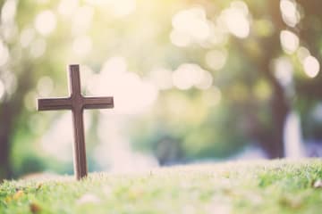 A cross stands alone in an empty grass field