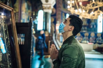 Man has mask on looking up and is praying