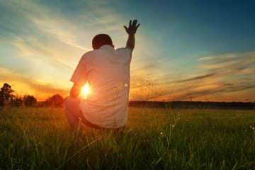 Man prays to God in grassfield 