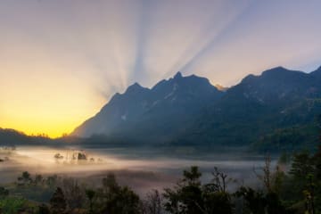 The sun rises behind a mountain backdrop