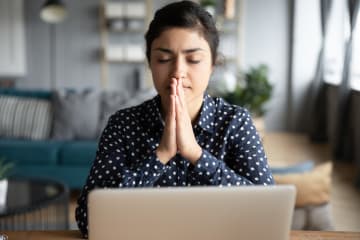 Woman in blue and white polka dot button-down shirt praying at work