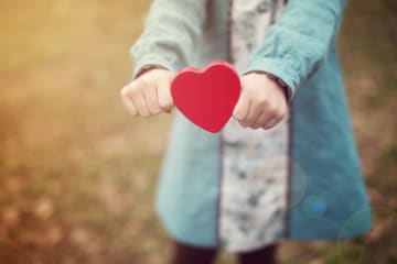 Woman holds out a cutout in the shape of a red heart