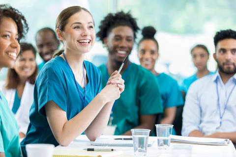 Group of diverse students in healthcare attire attending a classroom session in a public health degree program.
