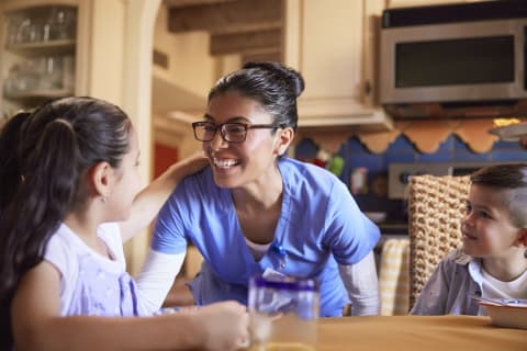 Female nurse wearing scrubs while smiling with young kids in home kitchen