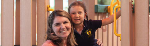 Teacher smiling with young student outside on a playground set