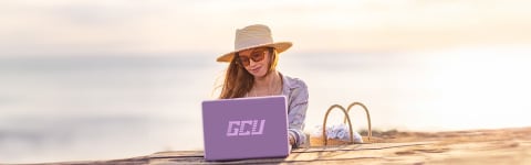 Female GCU student completing online degree coursework at beach in FL