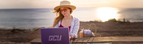 Female GCU student completing online degree coursework at beach in CA
