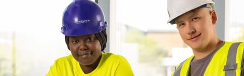 Man and woman in pre-apprenticeship program wearing hard hats and yellow safety vests