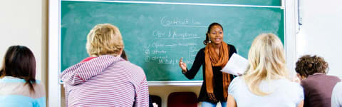 teacher standing by blackboard teaching students in classroom