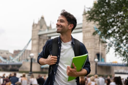 Young man in a foreign city holding a notebook and backpack