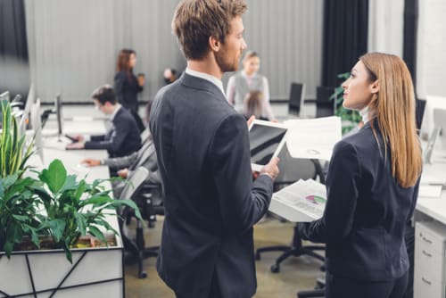 Business woman and man talking in a busy office setting 