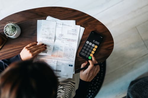 Person entering numbers in a calculator while holding papers in other hand