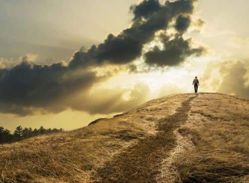 Person walking on a hill with the cloudy sky in the background