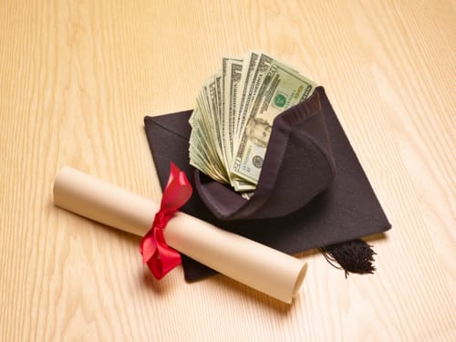 Rolled diploma and graduation cap with dollars inside