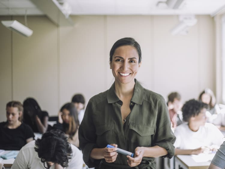 female teacher smiling while students study behind her