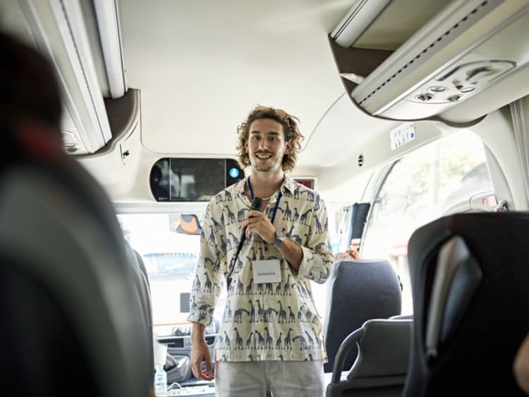 A male tour guide talking with passengers on bus