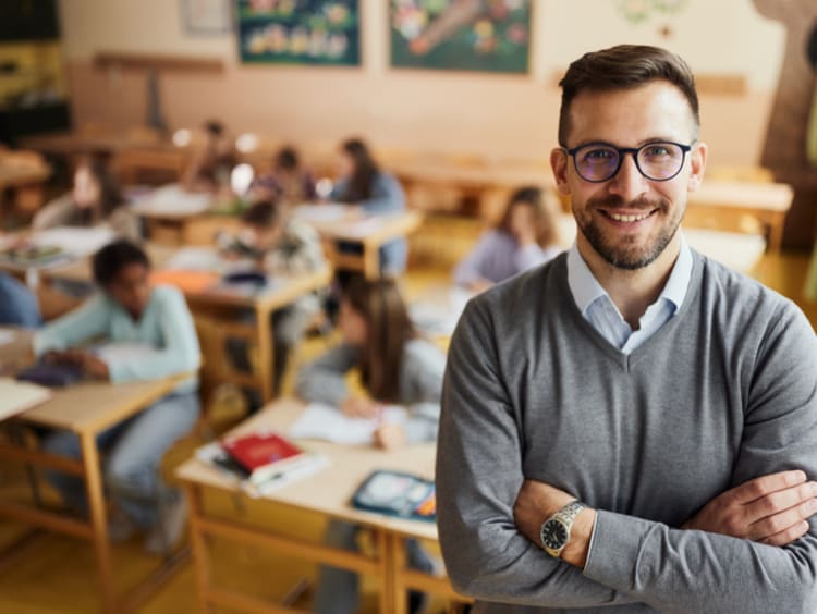 Smiling male teacher standing in front of elementary classroom