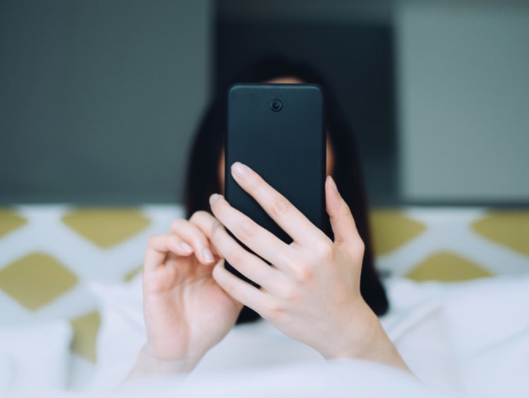 Woman sitting in bed scrolling on the phone