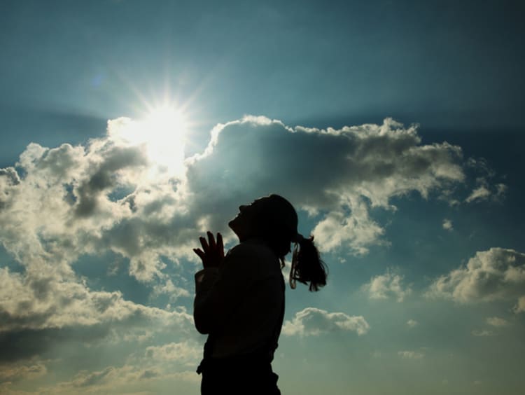 Female praying and looking up to the sky and sun