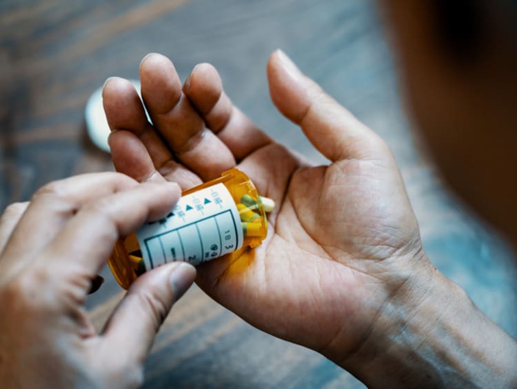 Close-up of a male hand holding a pill bottle pouring medication into his hand - stock photo