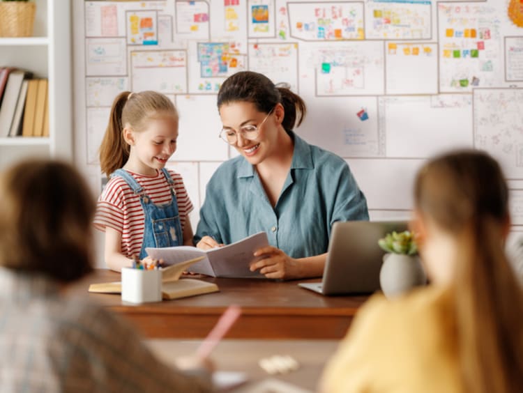 Elementary teacher talking with student at desk