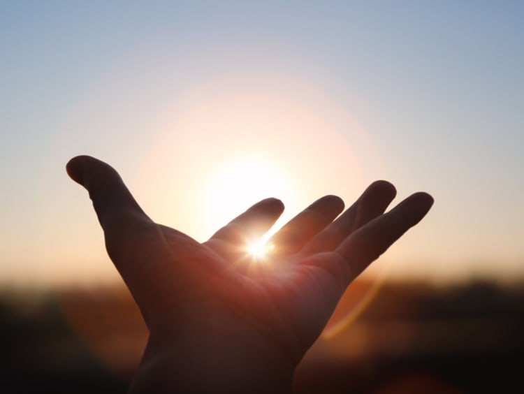 hand stretched toward sunrise with light peaking through