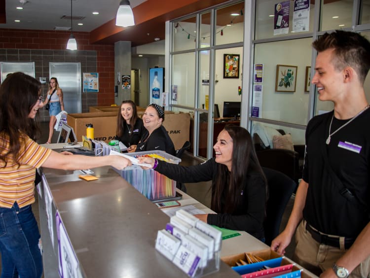 Student handing a paper to a person sitting down to apply to GCU.