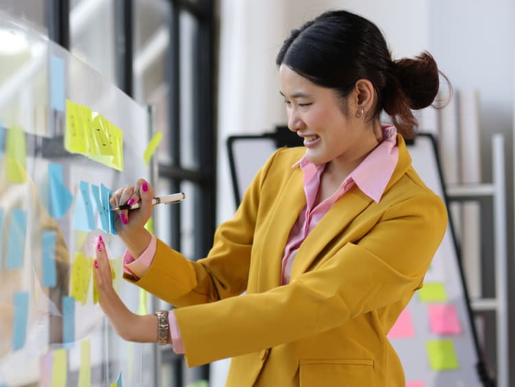 Woman brainstorms on a board with sticky notes.