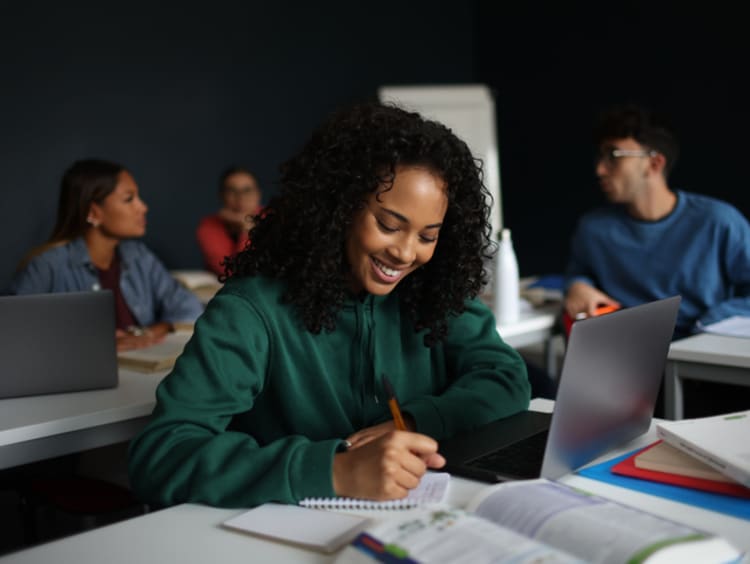 young female student smiling while writing in notebook
