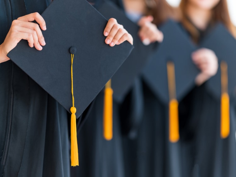 Graduating students in graduation gowns holding their caps